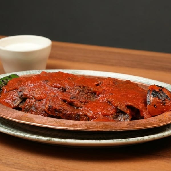 Iskender kebab with tomato sauce, grilled pepper, and tomato, served with a side of ayran.