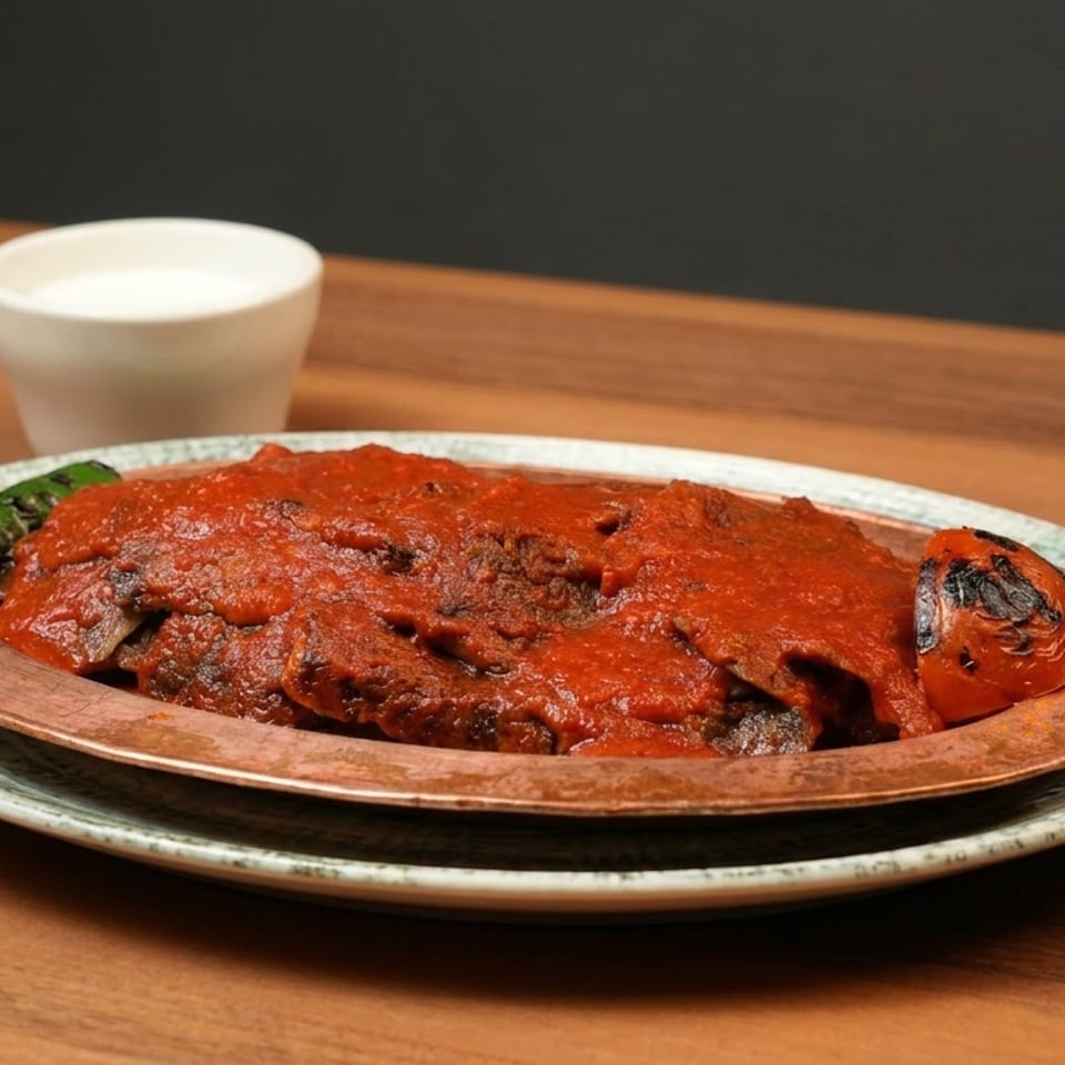 Iskender kebab with tomato sauce, grilled pepper, and tomato, served with a side of ayran.