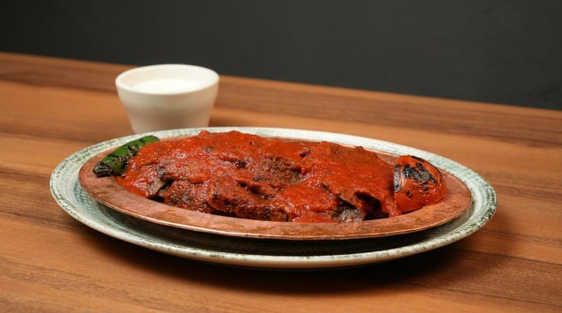 Iskender kebab with tomato sauce, grilled pepper, and tomato, served with a side of ayran.