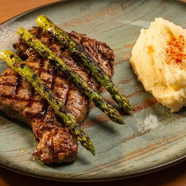 Grilled steak with asparagus and a side of mashed potatoes on a rustic plate.