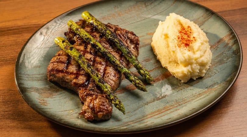 Grilled steak with asparagus and a side of mashed potatoes on a rustic plate.