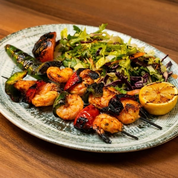 Grilled shrimp and vegetable skewers with a side salad and a grilled lemon half on a plate.