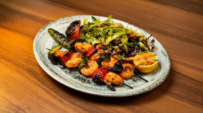Grilled shrimp and vegetable skewers with a side salad and a grilled lemon half on a plate.